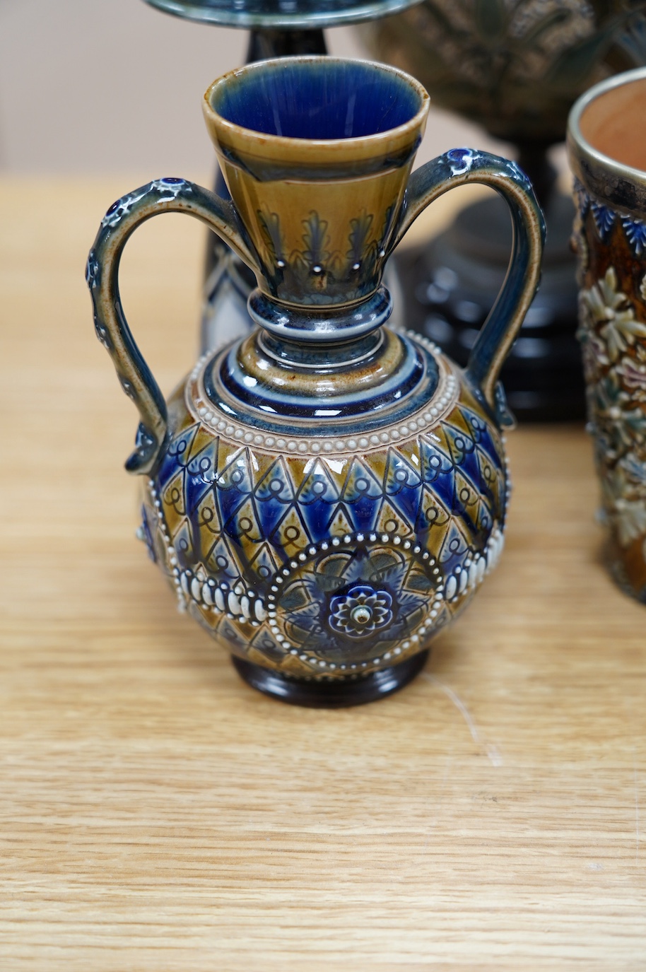 Seven Royal Doulton mixed vases etc, including two candlesticks, a pair of vases, a beaker, etc, tallest 21cm. Condition - the two handled pedestal jar has lost its lid, the other items are good